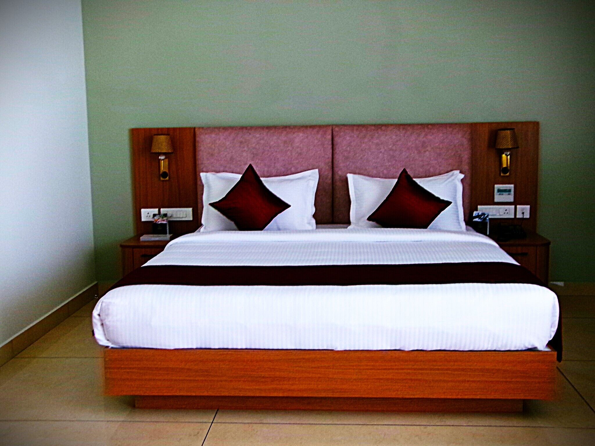 A large bed with a wooden frame, two nightstands with lamps, and a green wall.
