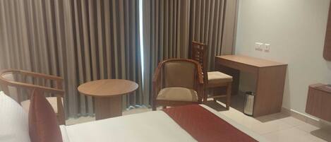 Habitación de hotel con cama, escritorio, silla, mesita y cortina.