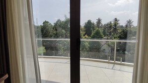 Un balcón con barandilla de cristal, suelo de baldosas y vistas a árboles y edificios.
