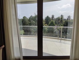 Un balcon doté d’une balustrade en verre, d’un sol carrelé et offrant une vue sur les arbres et les bâtiments.