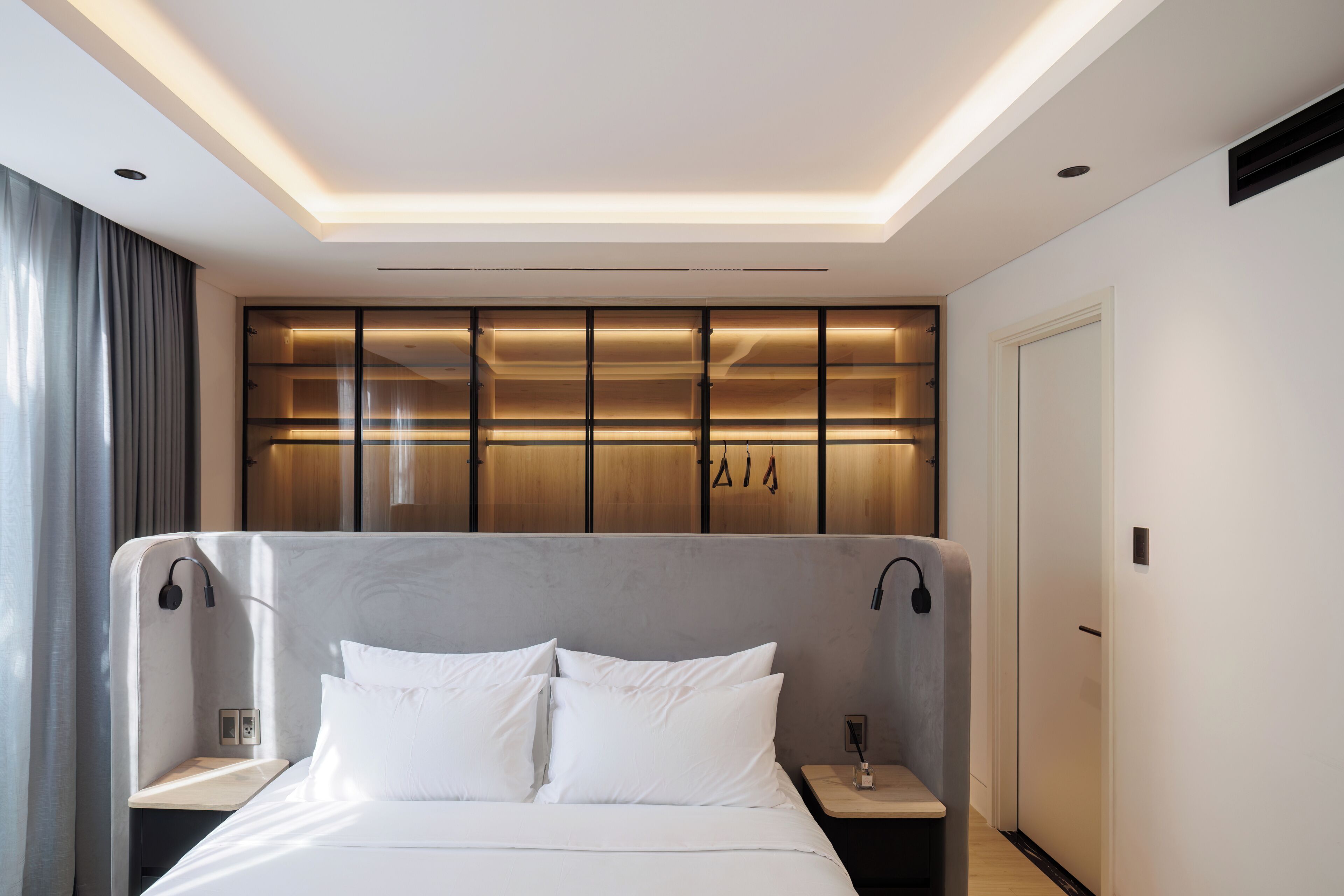 A modern hotel room with a large bed, bedside tables, a wardrobe with illuminated panels, and a ceiling light fixture.