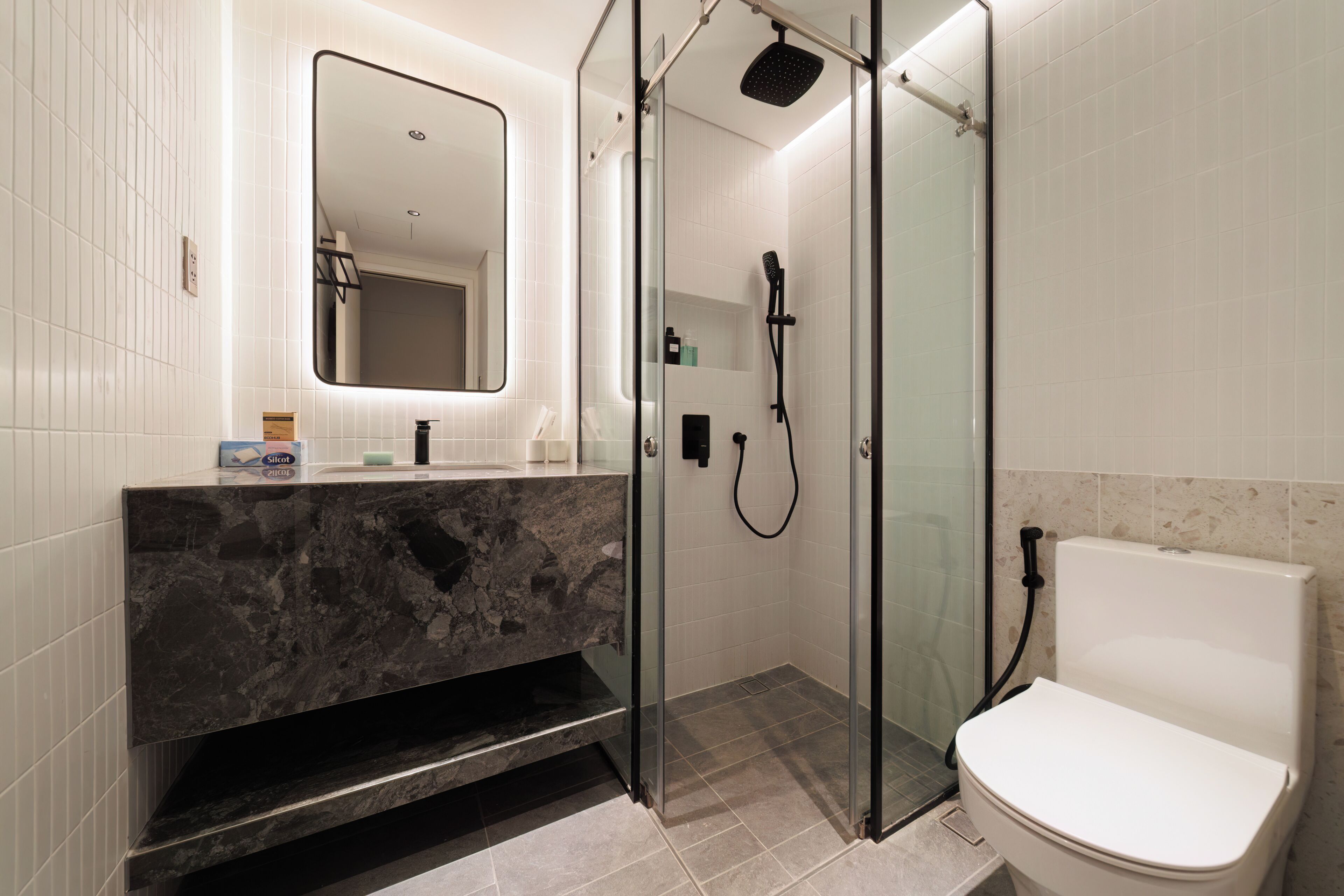 Ein modernes Badezimmer mit einer gläsernen Duschkabine, einem Marmorwaschtisch und einer weißen Toilette.