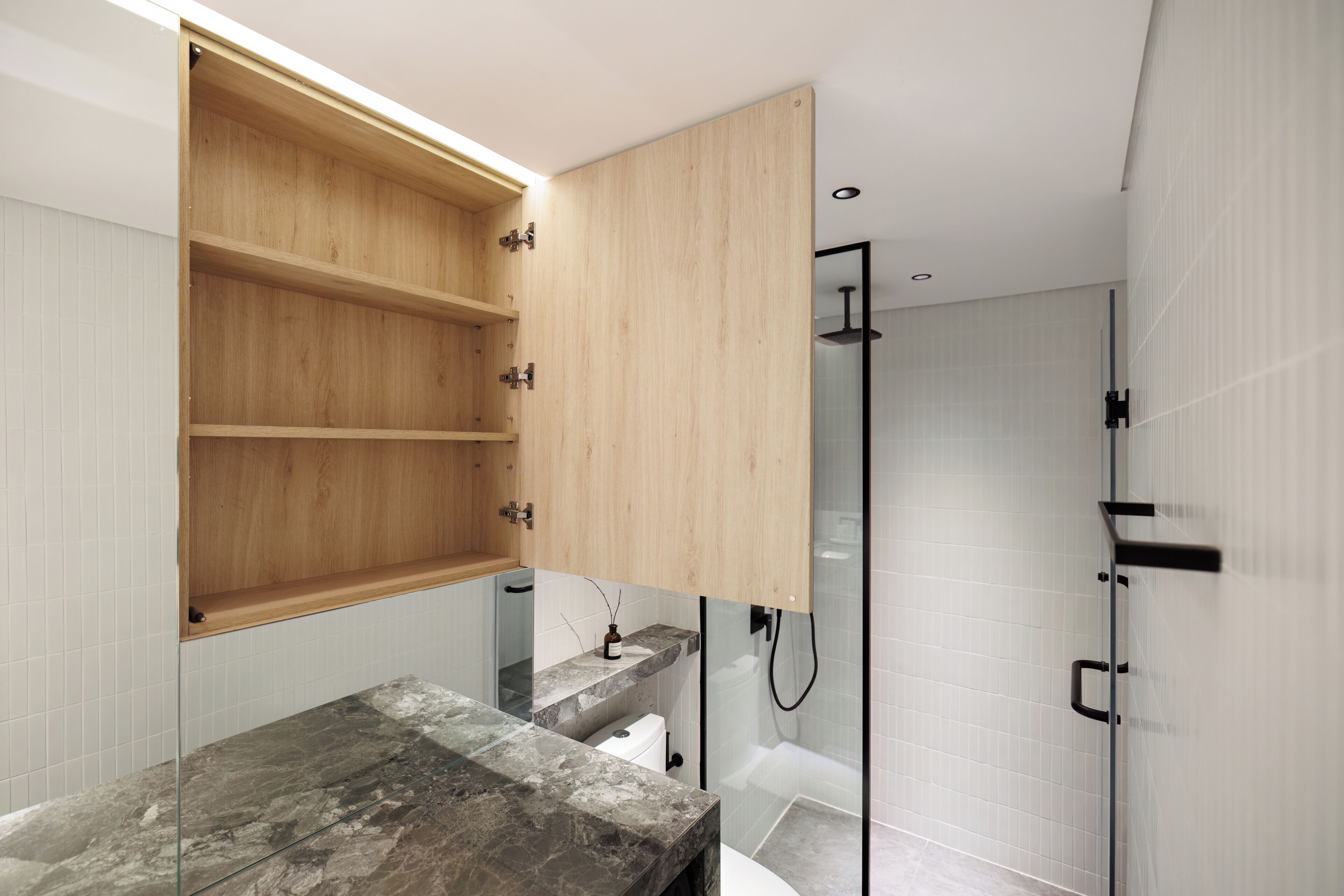 Un baño moderno con un armario de madera, encimera de mármol, cabina de ducha de vidrio y paredes con azulejos blancos.