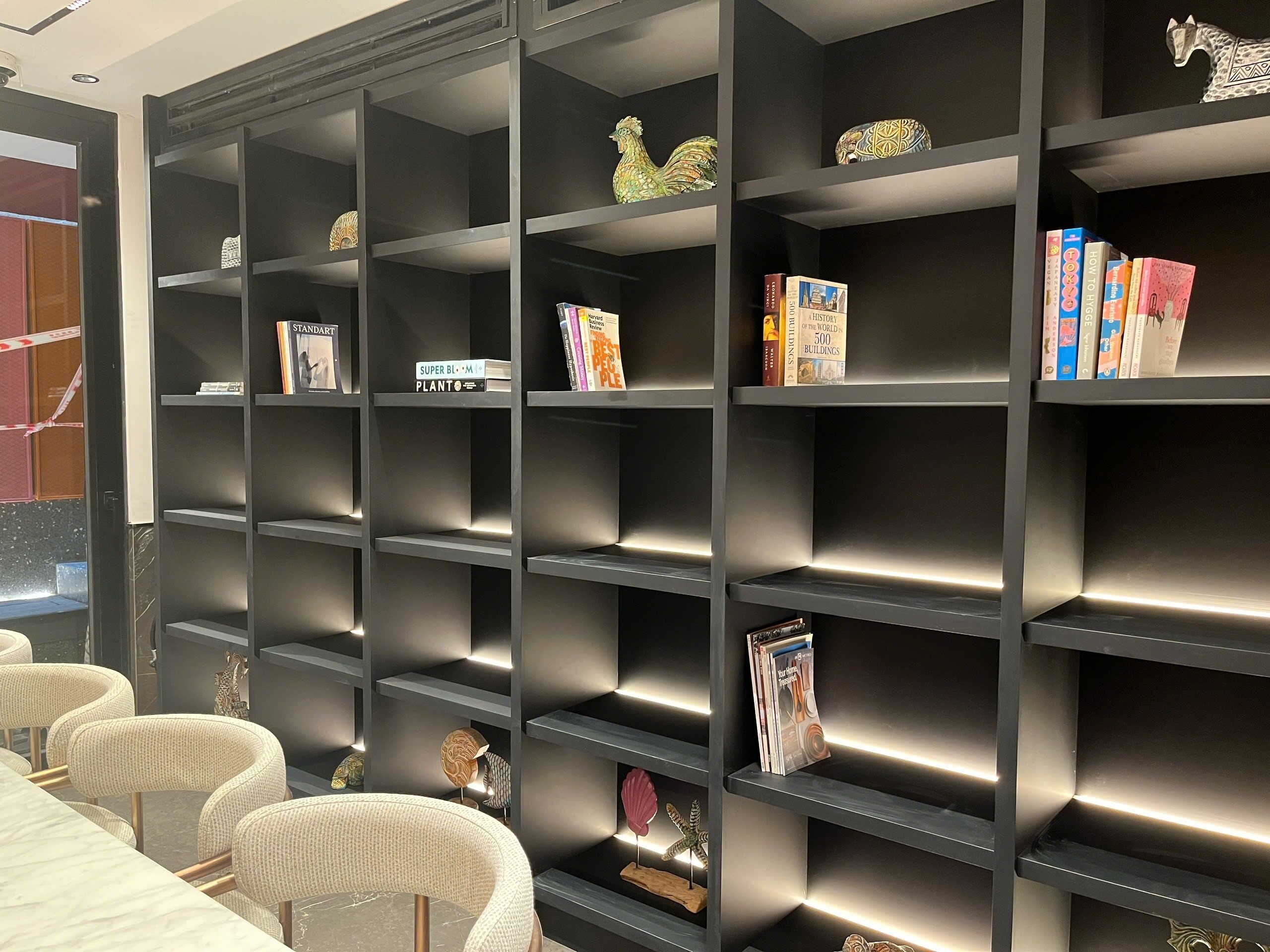 Una biblioteca moderna con estanterías, elementos decorativos y una mesa de conferencias con sillas.