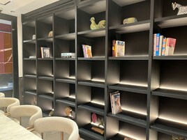 Una biblioteca moderna con estanterías, elementos decorativos y una mesa de conferencias con sillas.