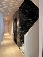 Un pasillo moderno con suelo de madera, paredes de mármol negro e iluminación empotrada.