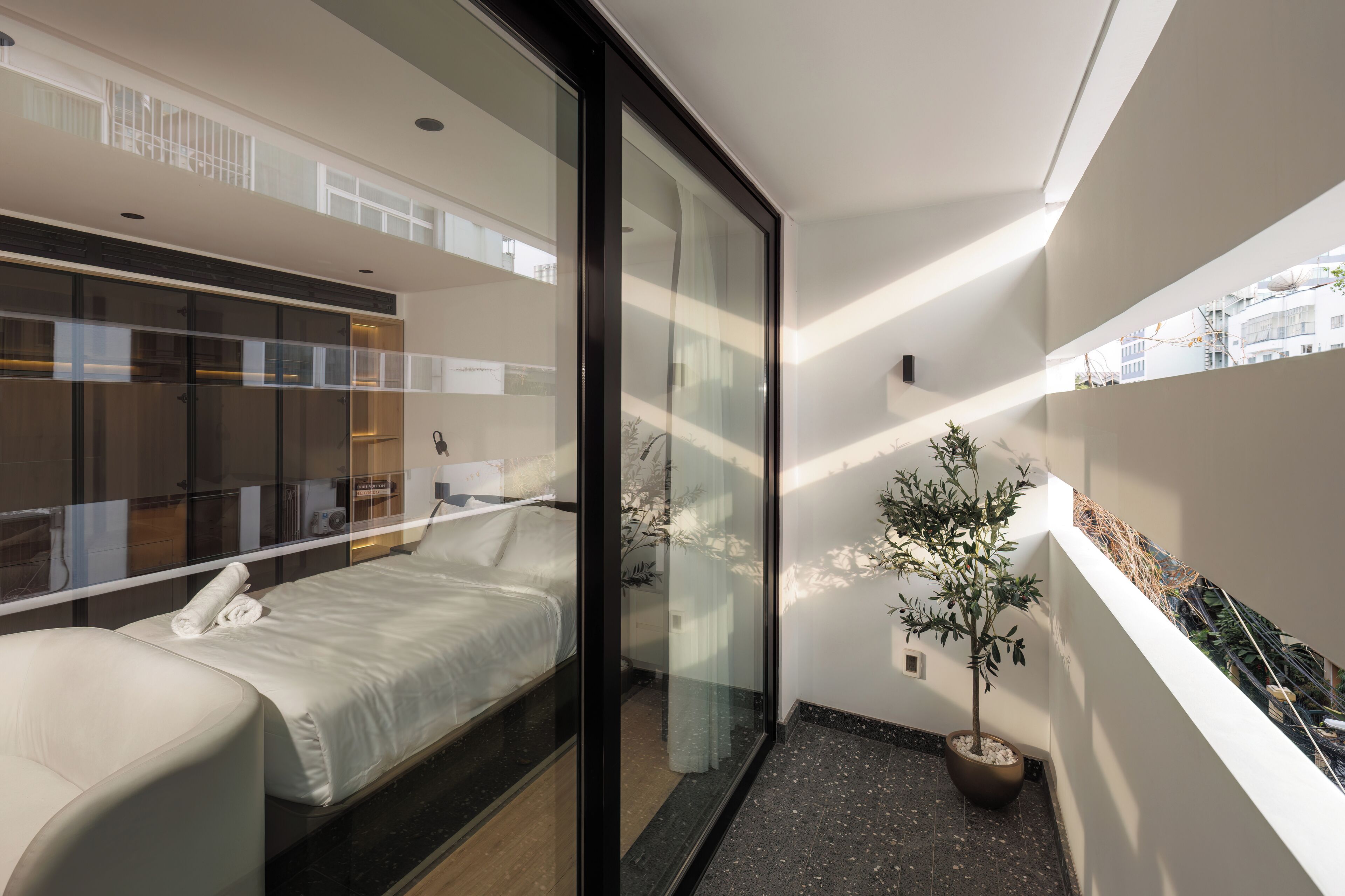 Ett modernt hotellrum med en säng, en glasvägg, en krukväxt och utsikt över staden.
