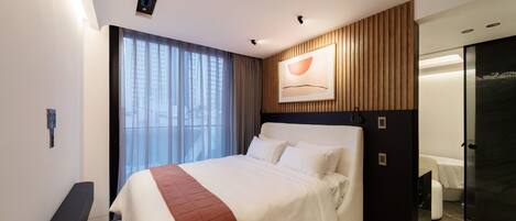 A modern hotel room with a large bed, a wooden panel wall, a painting, and a bathroom with a glass door.