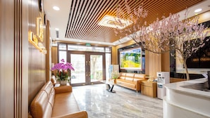 Eine moderne Lobby mit einer Rezeption, Ledersitzgelegenheiten, einem großen Bildschirm und einem Zierbaum.