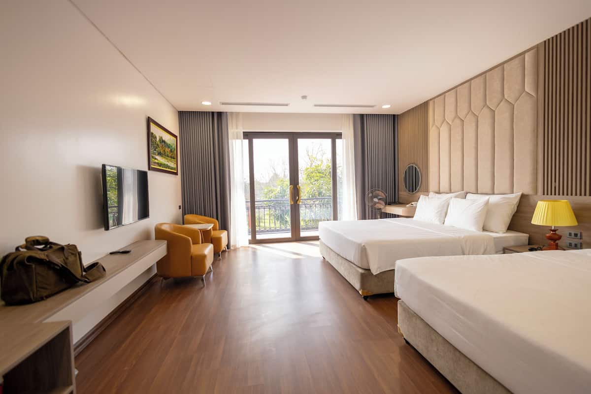 A hotel room with two beds, a sofa, a TV, and a balcony with a view.