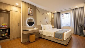 Ein Hotelzimmer mit Bett, Schreibtisch, Schminktisch mit Spiegel, Kleiderschrank und Fenster mit Vorhängen.