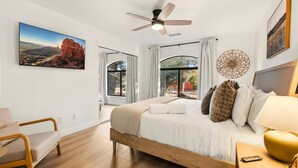 Une chambre à coucher avec un lit, un ventilateur de plafond, un bureau, une chaise et une grande fenêtre.