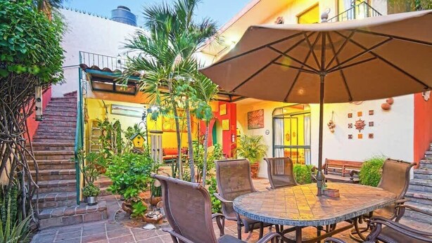 Une terrasse extérieure avec une table ronde et des chaises, entourée de plantes en pot et d’un escalier menant à un niveau supérieur.