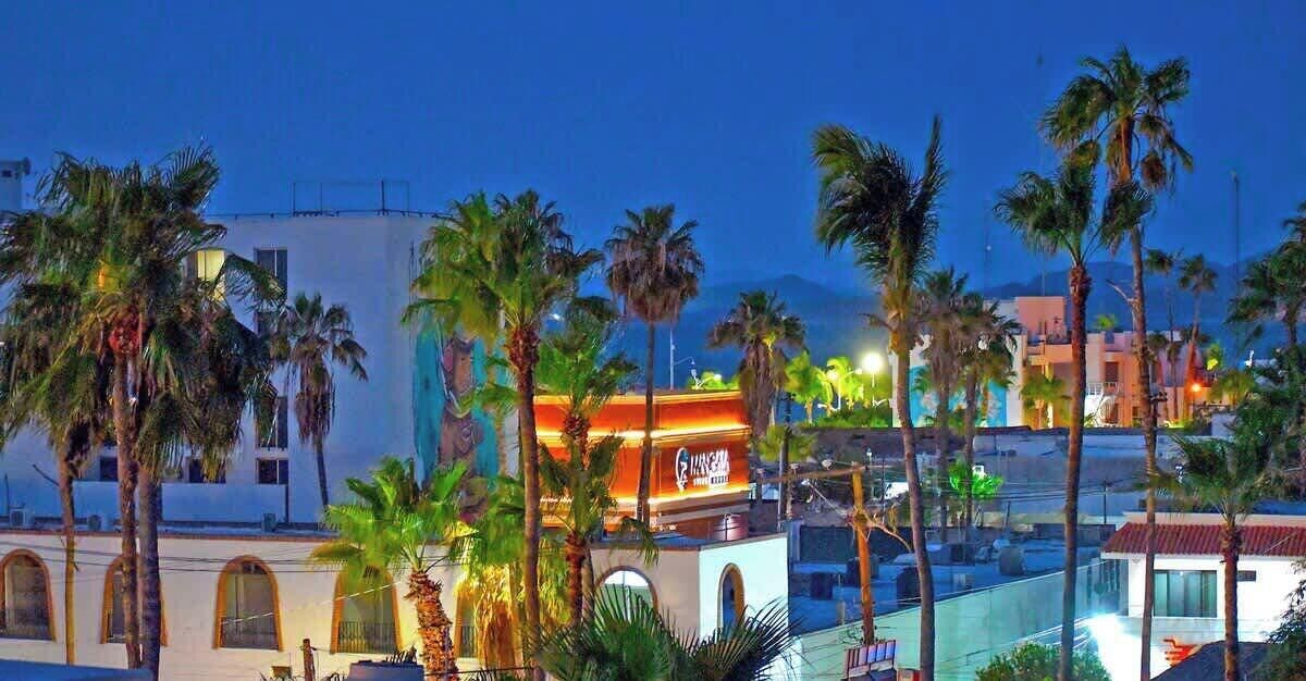 A hotel with a prominent sign, palm trees, and a mountainous backdrop.