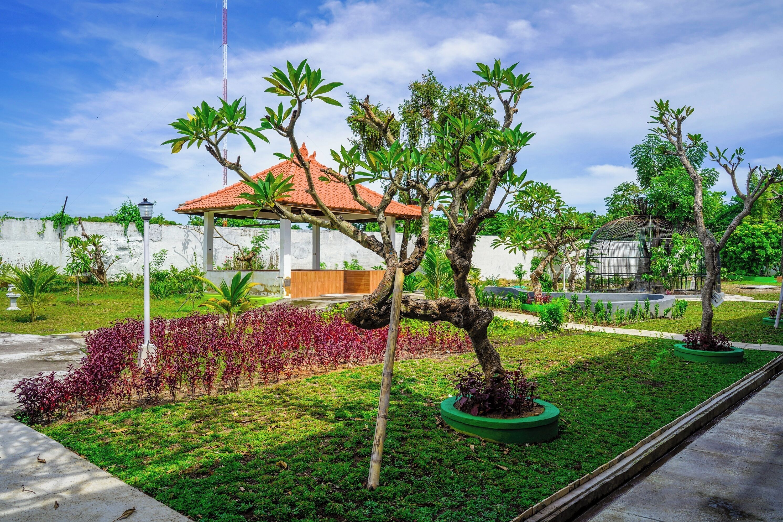 A garden with trees, a gazebo, and a building with a red roof.
