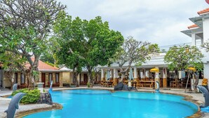 A swimming pool with surrounding lounge chairs and tables, a restaurant with outdoor seating, and a building with a tiled roof. - Grand Melka Hotel (Buleleng)