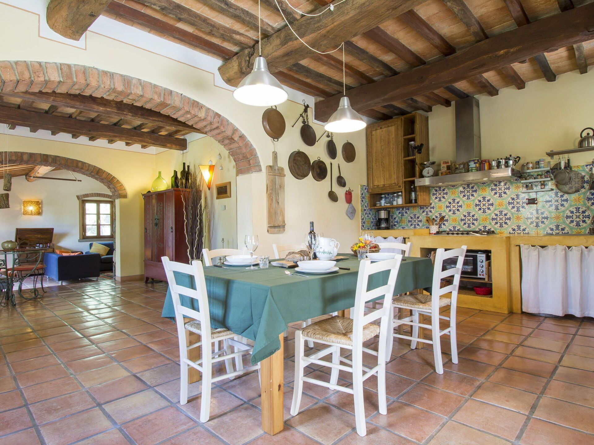 A dining area with a table set for four, surrounded by white chairs, under a wooden ceiling with exposed beams.
