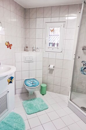 Een badkamer met toilet, wastafel, douche en een raam met een vlinderstickers.