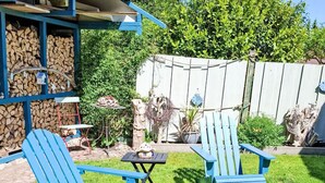 A backyard with two blue Adirondack chairs, a small table, and a wooden structure with a sloped roof. - Ferienbungalow auf Gartengrundstück by Interhome (Bad Doberan)