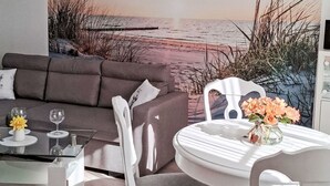 A modern living room with a sofa, a glass coffee table, and a dining area with a white table and chairs. - Ferienbungalow auf Gartengrundstück by Interhome (Bad Doberan)