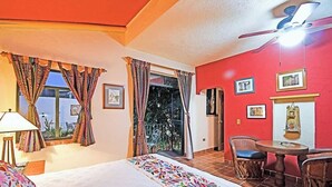A hotel room with a bed, a table with chairs, a ceiling fan, and a balcony with curtains. - Suite Steps from Malecon, Beach Dining Stripe (La Paz)