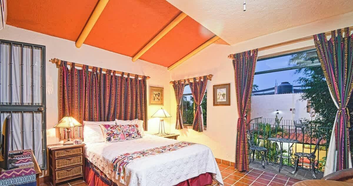 A bedroom with a bed, bedside tables, a balcony with chairs, and curtains.