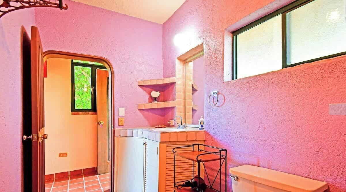 Une salle de bain avec un mur rose, une fenêtre, un lavabo, un miroir et un porte-serviettes.