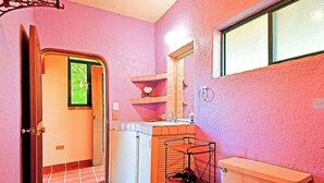 A bathroom with a pink wall, a window, a sink, a mirror, and a towel rack. - Suite Steps from Malecon, Beach Dining Stripe (La Paz)