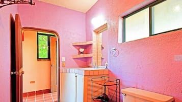 Une salle de bain avec un mur rose, une fenêtre, un lavabo, un miroir et un porte-serviettes.