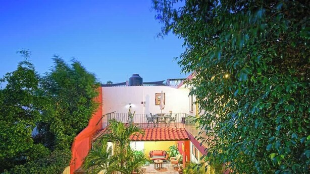 A courtyard with a red-tiled roof, a balcony with a table and chairs, and a water tank in the background. - Suite Steps from Malecon, Beach Dining Stripe (La Paz)