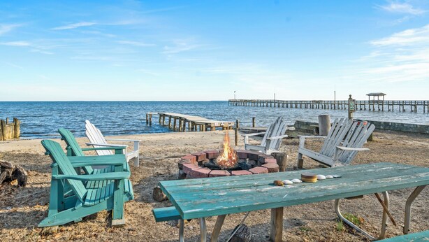 A beach with Adirondack chairs, a fire pit, and a wooden pier extending into the water. - Fabulous 5-bedroom house with AC in charming Port Republic. Walk to water/trail (Port Republic)