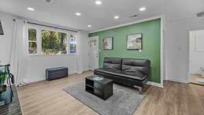 A modern living room with a black leather sofa, a small black coffee table, and a green accent wall. - Fabulous 5-bedroom house with AC in charming Port Republic. Walk to water/trail (Port Republic)