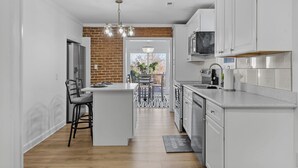 A modern kitchen with white cabinetry, a central island, and a brick accent wall. - Fabulous 5-bedroom house with AC in charming Port Republic. Walk to water/trail (Port Republic)
