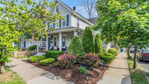 A two-story house with a front porch, a well-maintained garden, and a sidewalk leading to the street.