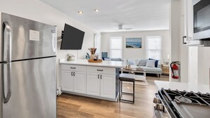 A modern kitchen with a stainless steel refrigerator, a flat-screen TV, and a gas stove.