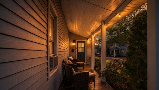 A covered porch with wooden siding, a door, and a seating area with chairs and a table.