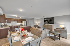 A modern kitchen with dark wooden cabinets, a dining area with a table set for four, and a living area with a sofa and a TV mounted on the wall. - Modern Birmingham Retreat (Birmingham)