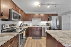 A modern kitchen with stainless steel appliances, wooden cabinets, and a marble countertop. - Modern Birmingham Retreat (Birmingham)