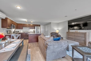 A modern kitchen with built-in appliances, a dining area with a long table set for two, and a cozy living space with a sofa and a TV. - Modern Birmingham Retreat (Birmingham)