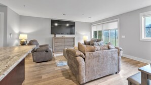 Una sala de estar moderna con un sofá, un sillón reclinable, un televisor montado en la pared y un ventanal grande.