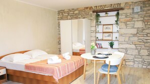 A bedroom with a bed, a bedside table, a chair, a round table, and a stone wall with a shelf.