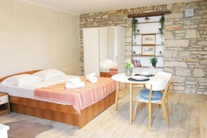 A bedroom with a bed, a bedside table, a chair, a round table, and a stone wall with a shelf.