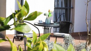 A patio with a round table, two chairs, a vase with flowers, and a window with bars.