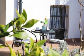 A patio with a round table, two chairs, a vase with flowers, and a window with bars.