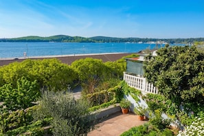 A balcony with a view of a lake, surrounded by greenery and a white fence. - Apartment Akidado - Garden & Sea View (Pula)