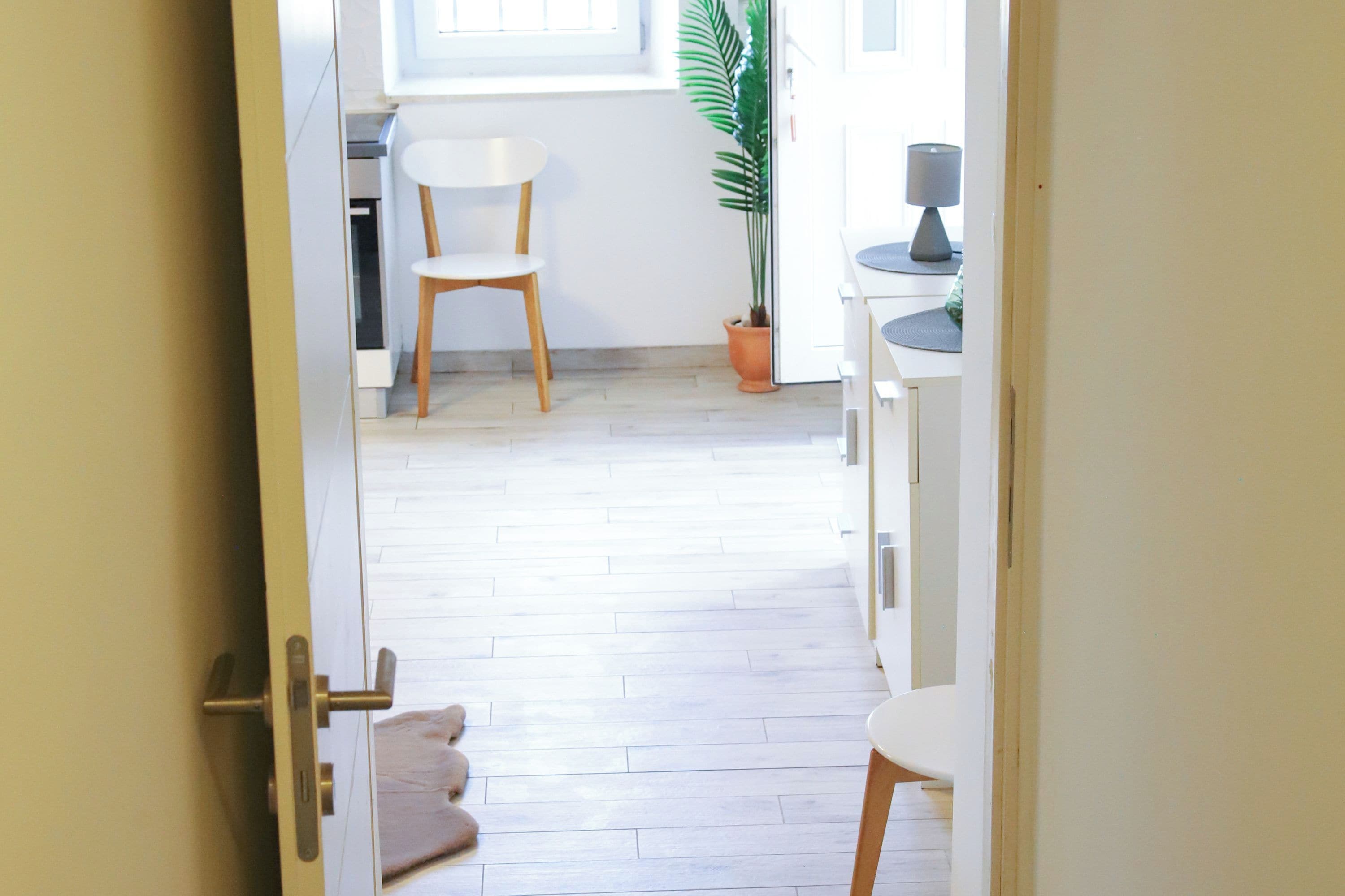 A doorway leading to a room with a white chair, a potted plant, and a lamp on a table.