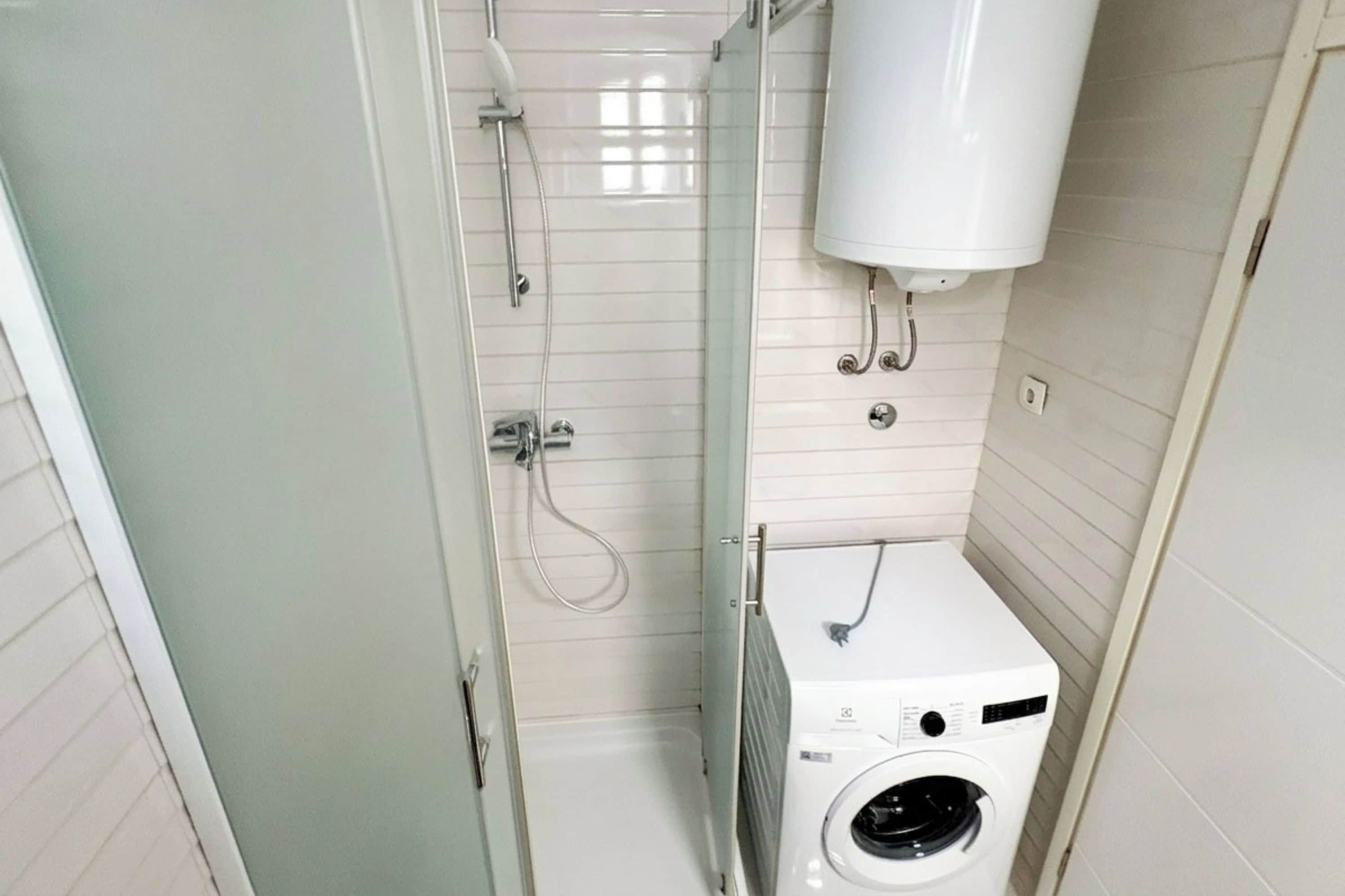 A compact bathroom with a glass shower enclosure, a built-in washing machine, and a white toilet.