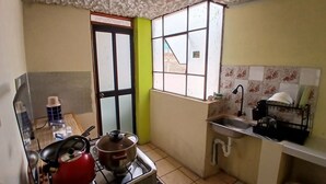 Une cuisine compacte équipée d’une cuisinière à gaz, d’une bouilloire rouge, d’un évier et d’une fenêtre donnant sur un paysage agréable.
