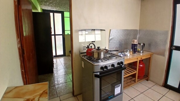 Une cuisine de taille réduite, équipée d’une cuisinière à gaz, d’un petit plan de travail et d’une bouteille de gaz.