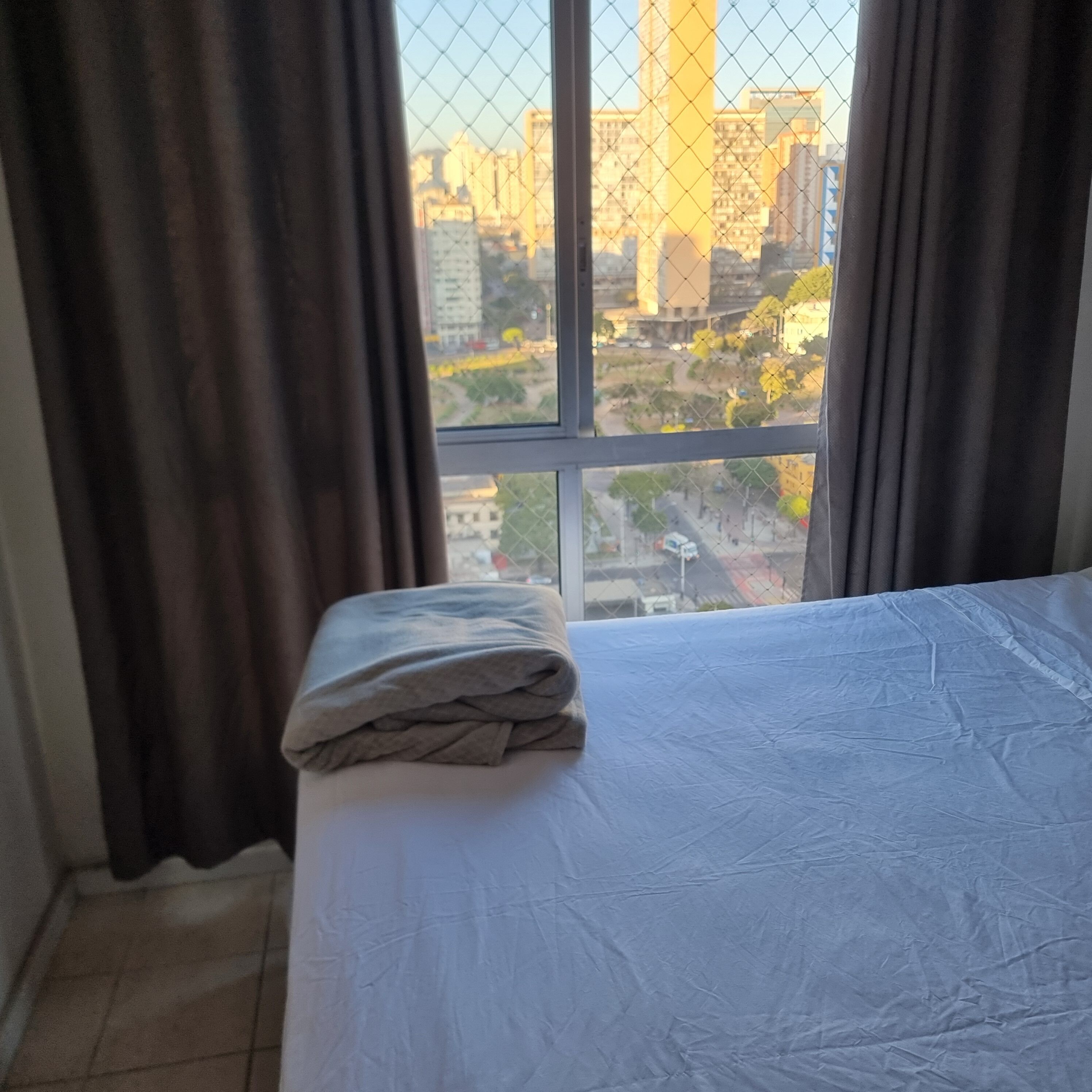 Quarto de hotel com cama, cortinas e vista para a cidade.